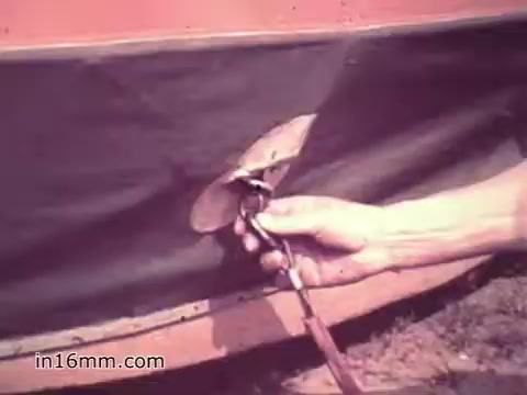 The still from 'Your Man in Nürnberg' features a close-up of a hand using a tool to work on mechanical equipment, likely related to the supply and maintenance responsibilities of a U.S. Army Specialist. The context suggests a focus on Joe Naifus's technical skills and the complexities of his job in the Army, emphasizing both the challenging nature of his work and the training he received. The scene captures a moment of hands-on maintenance, reflecting the dedication required in military roles.