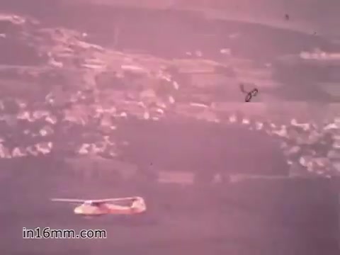 The still from the PSA 'Your Man in Nürnberg' features a helicopter in flight, likely part of the U.S. Army's operations. The background shows a hilly landscape with small villages, indicative of the German countryside. The image captures a moment of military activity while hinting at the scenic environment that surrounds Joe Naifus's experience as a Specialist four in the Army, blending the themes of duty and exploration.