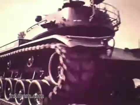The still from the 1960s US Army recruiting PSA 'Your Man in Nürnberg' showcases a military tank, emphasizing the complexity and scale of army machinery. The focus is on Joe Naifus, a Specialist Four responsible for overseeing the supply and maintenance of various parts essential for the tank's operation. The scene illustrates the hectic yet important nature of his job in the Army, while also hinting at the balance of work and leisure, as Joe enjoys sightseeing in Nürnberg after his responsibilities.