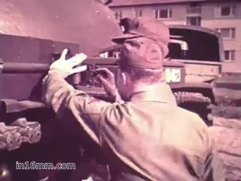 The still from 'Your Man in Nürnberg' depicts a soldier, likely Specialist Four Joe Naifus, working on a military vehicle. He is focused on a component of the tank, demonstrating the technical and hands-on nature of his supply job in the U.S. Army. The background shows military barracks or vehicles, emphasizing the military environment. This PSA highlights the skills and responsibilities of Army personnel while also hinting at their leisure time in the city.