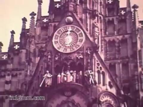 The still from the US Army recruiting PSA 'Your Man in Nürnberg' features a Gothic-style clock tower, likely part of a historic cathedral or building, situated in Nuremberg. The clock's face is prominent, framed by intricate architectural details and figures, suggesting a scene of historical significance. The image alludes to the cultural and historical richness of Nuremberg, contrasting with the military focus of the PSA. This juxtaposition highlights the balance between duty and exploration experienced by soldiers like Specialist Joe Naifus.