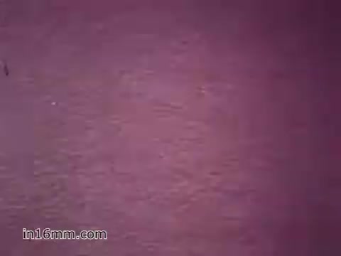 The 16mm still from the US Army recruiting PSA 'Your Man in Nürnberg' features a close-up view with a muted, possibly reddish background. The context highlights Joe Naifus, a Specialist Four in the Army, who manages the complexities of supply logistics. The narration emphasizes the demanding nature of his role while showcasing the skills and training he received from the Army. After work, Joe enjoys sightseeing, emphasizing a balance between duty and leisure.