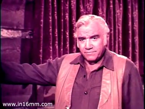 The still from the 1968 PSA features Lorne Greene, dressed in a rugged outfit with a western-style vest. He appears to be speaking directly to the audience with a serious expression, emphasizing the importance of overseas aid. The background has rich, deep colors, likely red curtains, suggesting a dramatic setting. His posture and gaze imply an authoritative presence, typical of the character he portrayed in 'Bonanza.' The impression of him reading from cue cards aligns with the structured delivery of his message.