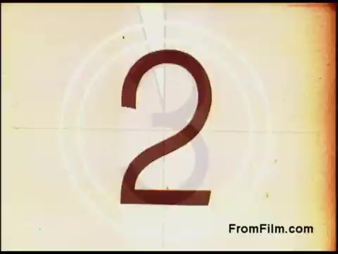 The still features a vintage countdown graphic from a 16mm film, specifically from the Bell System in the 1970s. It showcases the number '2' prominently in a retro style, surrounded by concentric circles typical of old film countdowns. The background has a warm, faded color with visible film grain, suggesting age and authenticity. The overall look evokes nostalgia for classic filmmaking techniques.