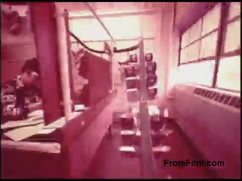 The still from the 16mm film features a setting typical of an office environment from the 1970s, likely depicting a telephone system, given its origin with Bell System. The image showcases a work area with desks, a window allowing natural light, and a figure engaged in tasks at a desk. There appears to be a transparent screen or display in the foreground, adding a layer of depth and suggesting a focus on communication technology. The overall color tone leans towards a warm, reddish hue, characteristic of the film's age.