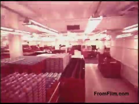 The still showcases a spacious, well-lit storage facility filled with organized rows of boxes and items. The interior has a utilitarian design typical of industrial settings, with bright overhead lights illuminating the area. The boxes appear to be neatly arranged, indicating a systematic approach to storage, possibly related to telecommunications, given the film's association with Bell System. The overall ambiance reflects a functional workspace from the 1970s era.