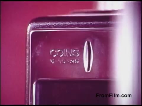 The 16mm still from the 'Bell System Film from the 1970s' features a close-up of a coin slot on a payphone. The metal surface is reflective, and the inscription clearly reads 'COINS' along with the denominations of '5, 10, 25'. The background appears to be a soft focus with a warm hue, typical of the film's era, creating a nostalgic feel.