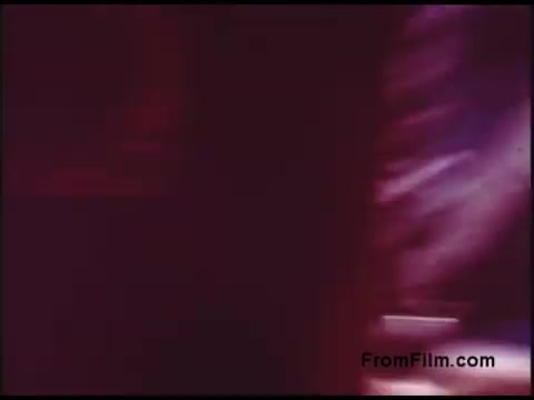 The 16mm still from the 'Bell System Film from the 1970s' captures a blurred and abstract scene with rich colors and soft lighting, characteristic of the visual style of that era. The composition has an atmospheric quality, suggesting movement or activity, likely related to telecommunications. Details are indistinct, evoking a sense of nostalgia and the historical context of Bell System's contributions to technology.