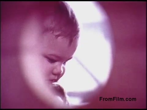 The still from the 1970s Bell System film features a close-up of a child's face, emphasizing their focused expression. The image has a soft, dreamlike quality, with a pinkish hue giving it a nostalgic ambiance. There seems to be a circular framing effect, which draws attention to the child's features and contemplative demeanor. The background appears blurred, enhancing the subject's prominence.
