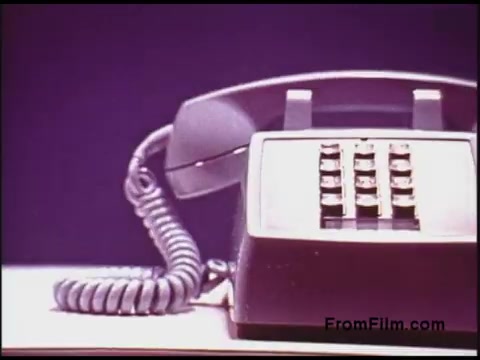 The still features a classic 1970s rotary dial telephone, prominently displayed against a simple backdrop. The telephone has a coiled cord and a numeric keypad, reflecting the design aesthetics of that era. The image has a vintage quality, characteristic of 16mm film, showcasing a nostalgic theme related to communication technology from that time period.