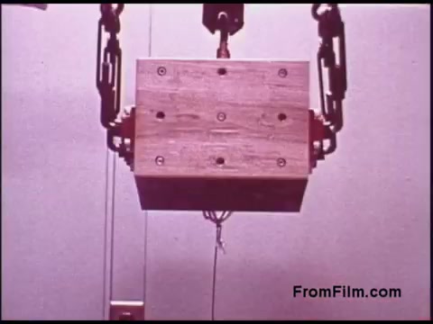 The still shows a mechanical setup featuring a wooden box being lifted by a crane-like apparatus. The box is suspended by a cable, and the scene is likely part of a demonstration or experiment, possibly related to engineering or telecommunications, given its connection to Bell System films from the 1970s. The focus appears to be on the mechanics of lifting and stability.