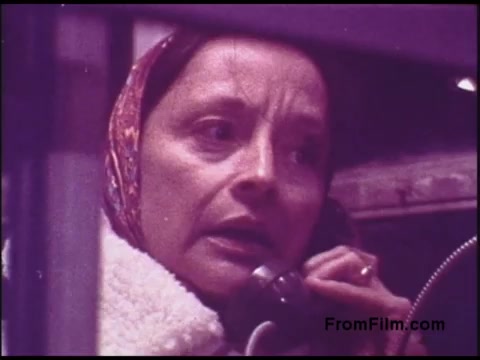 The still features a woman in a headscarf, appearing concerned while speaking on a telephone. Her expression conveys intensity or urgency, set against a slightly blurred background. The color palette has a vintage hue, typical of 1970s film, contributing to a nostalgic or historical feel. This image captures a moment that likely reflects personal or social themes prevalent in that era.