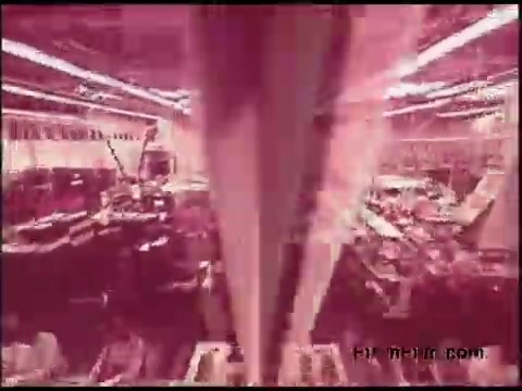 The still from the 'Bell System Film from the 1970s' features a vibrant, pink-tinted image capturing a busy technological environment. It appears to show numerous pieces of equipment and machinery aligned in an industrial setting, likely related to telecommunications. The visual conveys a sense of activity and innovation typical of that era's telecommunications advancements.