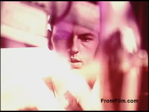 The still from the 1970s Bell System film captures a focused individual, likely engaged in a technical or operational task. The image features a blend of soft focus and color distortion, creating a dreamy quality that emphasizes the subject's concentration. The surrounding equipment suggests a setting related to telecommunications or technical processes, common themes in Bell System productions during that era.