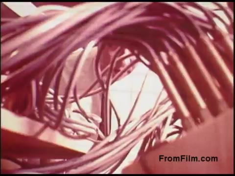 The 16mm still from the 'Bell System Film from the 1970s' shows a close-up view of tangled wires and cables, highlighting the intricacies of telecommunications infrastructure. The warm, muted colors suggest an aged film quality, reflecting a period when such technology was evolving. This shot may emphasize the complexity and interconnectedness of the systems used in communication at that time.