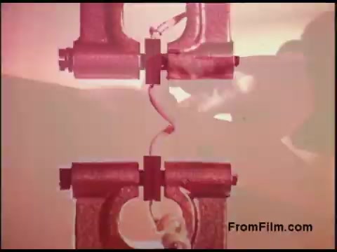 The still depicts a close-up of a mechanical component, likely part of a telecommunications system, set against a faintly blurred background. The image emphasizes the intricate details of the component, with a red tint that adds a distinctive aesthetic characteristic of 1970s film. The scene suggests a focus on engineering or technical processes, which aligns with the typical themes of Bell System films from that era.