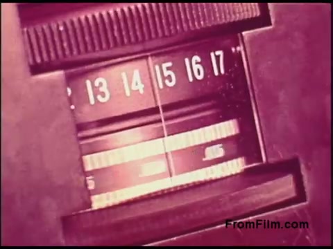 The still depicts a close-up of a vintage film projector or camera’s control panel, showcasing a numbered dial with markings from 13 to 17. The dials are set against a textured background, likely part of a mechanical device from the 1970s. The coloration appears slightly faded, giving it a nostalgic feel. The overall aesthetic reflects the era's design and technology related to film production.