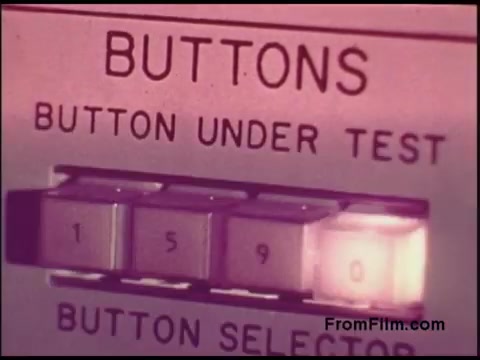 The still from the 16mm film 'Bell System Film from the 1970s' features a close-up of a control panel. It prominently displays a label reading 'BUTTONS' with the text 'BUTTON UNDER TEST' above a series of buttons. One button, labeled '1590,' is highlighted, possibly indicating an active selection. The overall aesthetic suggests a vintage technological setting, typical of that era's telecommunications equipment. The color tone appears slightly muted, characteristic of older film stock.