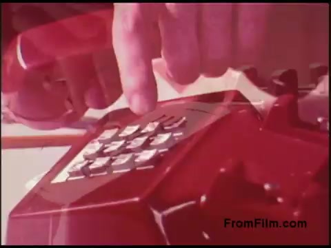 The still captures a close-up of a hand dialing a retro red rotary phone, characteristic of the 1970s era. The bright colors and focus on the phone's keypad highlight the technology of the time, likely emphasizing communication techniques or telephony in a broader context related to Bell's services. The image reflects both nostalgia and the design style of that decade.