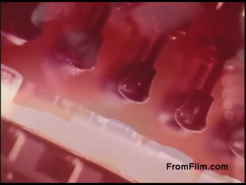 The still from the 16mm film depicts a close-up, abstract view of electronic components or mechanisms, likely highlighting technological elements associated with the Bell System. The image features a rich, warm color palette dominated by reds, enhancing the intricate details of the objects, which appear to be metallic or glass elements, possibly tubes or connectors. The composition suggests a focus on the inner workings of telecommunications technology from the 1970s.