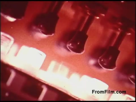 The still from the 16mm 'Bell System Film from the 1970s' features a close-up of various components, possibly electronic or mechanical parts, rendered in rich colors that evoke a vintage aesthetic. The image captures a sense of industrial design, with an emphasis on texture and detail, conveying the technology of that era. The lighting creates an atmospheric glow, adding to the retro feel of the piece.