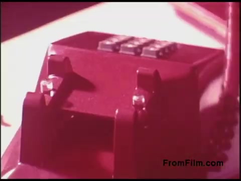 The still features a close-up of a vintage red telephone, presumably from the 1970s, showcasing its design and keypad. The lighting has a warm tone, emphasizing the retro aesthetic of the device. The focus is on the phone's details, highlighting the technology of that era.