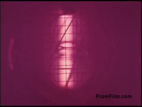 The still shows a close-up, monochromatic view of a tube or cylindrical object, suffused with a pink hue. The image features a grid-like pattern overlaying the central subject, which appears to be illuminated, likely indicating some form of scientific or technical equipment. This visual is characteristic of instructional or demonstration films from the 1970s, particularly related to telecommunications or electronics.