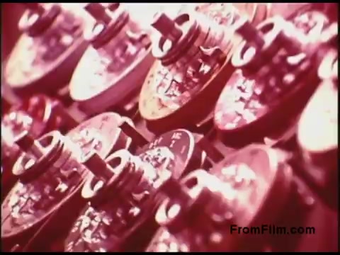 The still from the Bell System film features a close-up view of various components, likely from vintage telecommunications equipment. The image captures multiple rotary dials, displaying intricate details and a color palette dominated by warm tones. The focus on these mechanical parts suggests a theme related to technology or communication systems from the 1970s. The overall aesthetic reflects the era's design sensibilities.