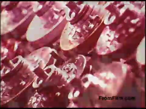 The still from the 16mm film 'Bell System Film from the 1970s' features a close-up view of intricate mechanical components, possibly related to telecommunications equipment or technology. The image has a warm, reddish hue, which adds a vintage feel. The focus on the metallic textures and shapes highlights the complexity and craftsmanship of the devices depicted. This captures a moment that reflects the technological advancements of that era.