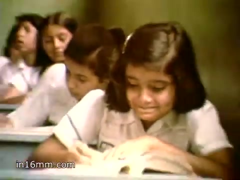 The still shows a classroom setting with young girls reading and engaged in their studies, likely representing the educational initiatives of Plan International. This 1980s PSA emphasizes the organization's mission to end poverty for children by promoting education and support. The atmosphere suggests focus and hope for a better future through learning.