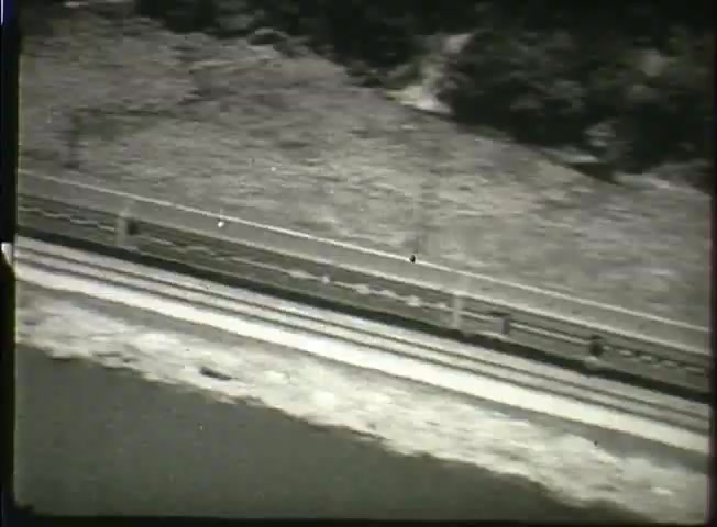 The still from 'Story Without End' presents an aerial view of a landscape with a road or railway track running alongside a body of water. The film, produced by Bell System in the late 1940s, likely showcases the infrastructure associated with telecommunications during that era. This scene may depict the physical layout relevant to the network's operation, emphasizing the connection of various locations and the surrounding natural environment. The overall tone is reflective of the period’s focus on technological advancement and the expansion of communication services.