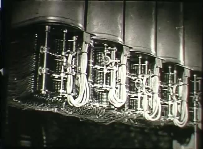 The still depicts intricate machinery from a Bell System central office, showcasing a series of interconnected components such as switches and wires. The focus on these technologies highlights the complexities of telephone networks in the late 1940s, illustrating both the hardware used for communication and the era's commitment to expanding telecommunication infrastructure. The design suggests a manual system, reflecting the technology of the time.
