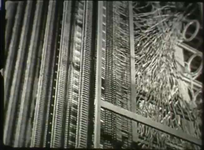 The still from 'Story Without End' depicts an intricate network of telephone switchboards, showcasing the complex wiring and operational mechanisms of the Bell System. The detailed arrangement highlights the technology in use during the late 1940s, illustrating the inner workings of a central office that facilitated telecommunications at the time. The image emphasizes both the sophistication and the foundational role of this equipment in connecting calls within the network.
