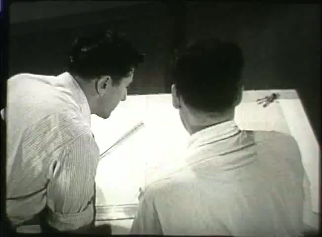 The still from *Story Without End* depicts two men closely examining technical drawings or blueprints on a table. Dressed in collared shirts, they appear engaged in a discussion, likely concerning telecommunications infrastructure, reflecting the Bell System's emphasis on network development in the late 1940s. The scene embodies a collaborative atmosphere, suggesting the intricacies of planning within the telecommunications industry during that era.