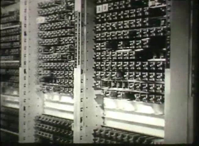 The still from 'Story Without End' showcases a close-up view of intricate telephone switching equipment, typical of the late 1940s Bell System technology. The image highlights several rows of metal circuits and connectors within a central office, illustrating the complexity of the network used for telephone communication during that era. The equipment appears meticulously organized, symbolizing the engineering precision involved in telecommunications at the time.