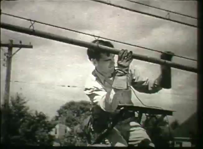The still from 'Story Without End' features a young man engaged in work on telephone poles, indicative of the telecommunications profession in the late 1940s. He is climbing or balancing on a platform while handling equipment, showing the physical demands of the job. The background includes power lines and trees, reflecting a suburban environment. The film likely conveys aspects of the Bell System's network operations and the essential role of linemen in maintaining communication infrastructure.
