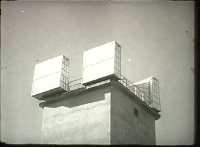 The 16mm still from 'Story Without End' features a concrete structure topped with large, rectangular devices. These appear to be antennas or communication equipment, typical of telecommunications infrastructure from the late 1940s. The backdrop is bright, suggesting a clear sky, which adds to the clarity of the scene. This still likely illustrates the technological advancements and network capabilities of the Bell System during that era.