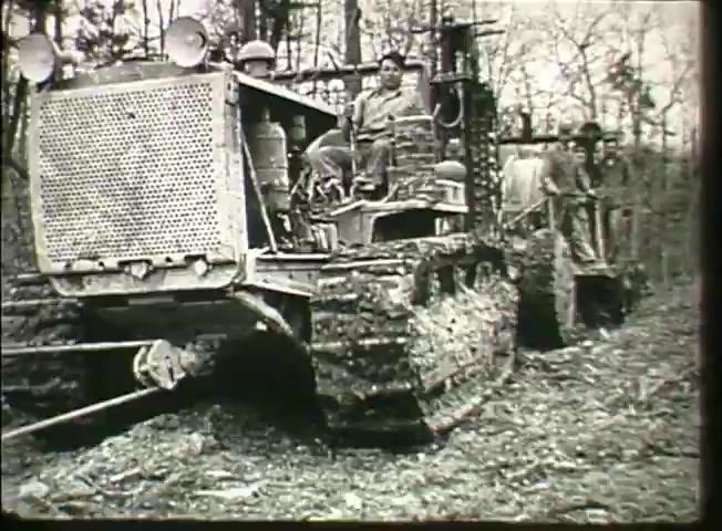 The still from 'Story Without End' features heavy machinery in a forested area, likely part of the Bell System's infrastructure development in the late 1940s. A bulldozer, operated by a man, is prominently in the foreground, while another piece of equipment is visible in the background. The scene emphasizes the effort in laying down communication networks, showcasing the rugged work environment and the technology of the era.