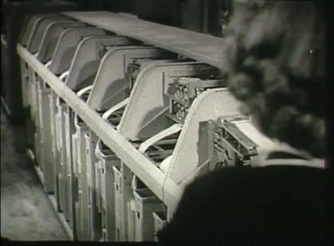 The still from 'Story Without End' showcases a series of equipment in a central office, typical of Bell System operations in the late 1940s. The image focuses on several large, machine-like components lined up, likely representing switching equipment essential for telephone network functionality. A partially visible figure suggests human oversight in this technological environment. The image highlights the industrial aesthetic of the era, emphasizing the blend of machinery and human effort in telecommunications.