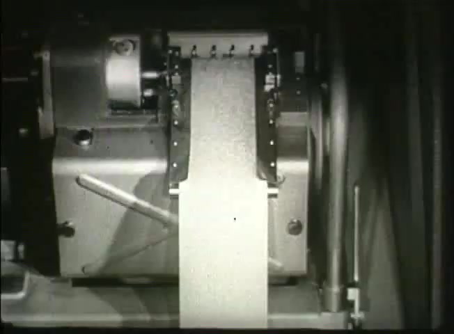 The still from 'Story Without End' features a close-up of a mechanical device, likely part of a telecommunications system. It shows a paper tape being processed, indicative of the technology used in the late 1940s for data transmission in the Bell System network. This imagery reflects the era's focus on communication advancements and central office operations.