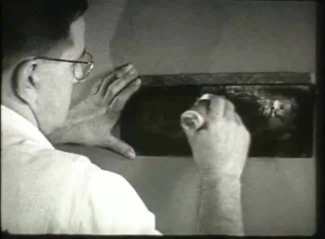 The still from 'Story Without End' depicts a technician applying paint or a similar substance to a surface, possibly for labeling or maintenance. The man is wearing glasses, suggesting attention to detail, and uses both hands for the task, indicative of careful workmanship. This scene likely relates to the operational aspects of the Bell System, reflecting practices related to network management and maintenance in the late 1940s. The film serves to showcase the technical diligence behind telephone network management during that era.