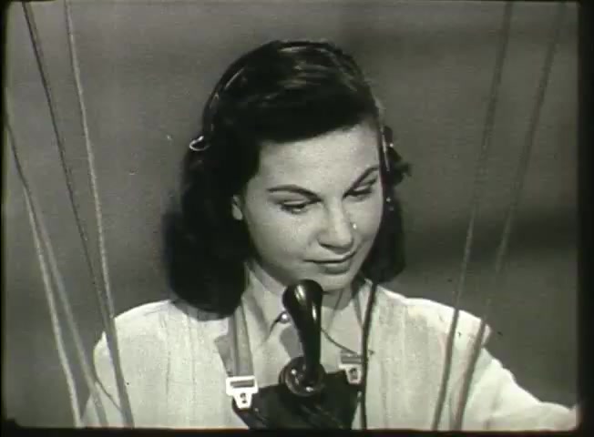 The still from 'Story Without End' features a young woman operating a telephone switchboard. She is focused on her task, wearing a headset and holding a telephone receiver. The setting likely reflects the mid-20th-century telecommunications environment, emphasizing the human aspect of communication before automation. The film captures a moment in the Bell System's history, showcasing the role of operators in connecting calls and managing the network at that time.