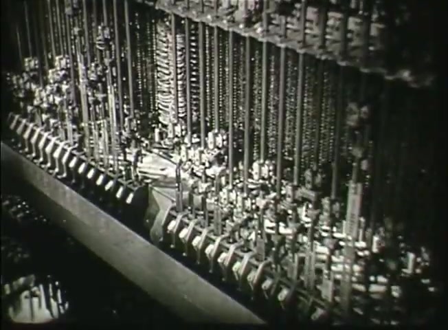 The still from 'Story Without End' showcases a close-up of vintage telephone equipment, likely from a central office, highlighting intricate mechanical components. The scene reflects the technology used in the late 1940s Bell System, illustrating the complexity of the network operations at that time. The focus on cogs and connections emphasizes the manual nature of telecommunications before the digital era.
