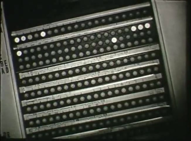 The still from 'Story Without End' depicts a close-up view of a section of a switching panel used in telecommunication. The panel features a grid of circular buttons, which likely represent connections or switches in a central office system. This image emphasizes the intricate technology of the Bell System in the late 1940s, illustrating the behind-the-scenes mechanism that facilitated telephone communication.