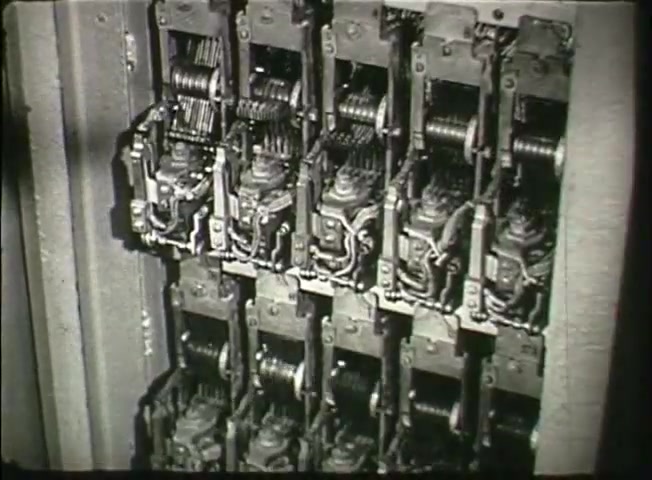 The still from 'Story Without End' depicts a close-up view of multiple telephone relays or switching mechanisms within a central office. The machinery features intricate metal parts, including coils and levers, indicative of the mid-20th century technology used by Bell System. This footage provides insight into the operational complexity of the telephone network during the late 1940s, showcasing how calls were processed and routed in a centralized telecommunication system.