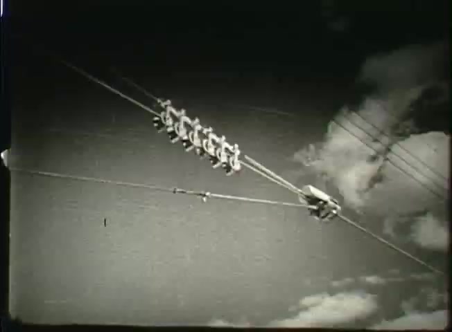 The still from 'Story Without End' showcases utility poles with several transmission wires, likely representing the communication infrastructure of the late 1940s. The black-and-white image captures the intersection of technology and nature, with clouds in the sky hinting at the setting's atmosphere. This visual element emphasizes the network's reach and complexity, reflecting the operations of the Bell System during that era.