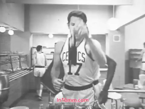 The still from the 1969 Diet Rite Cola commercial features John 'Hondo' Havlicek, a prominent player for the Boston Celtics. He is shown in a casual setting, likely a locker room or a dining area, wearing his Celtics jersey. He appears to be playfully promoting the Diet Rite Cola as he pours or showcases the drink. The atmosphere suggests a lighthearted and sporty vibe, typical of commercials from that era. The context of the ad highlights Diet Rite’s switch from cyclamate to saccharine as a sweetener, aiming to attract health-conscious consumers.