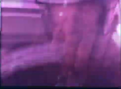 The still from the 'Last American Hero' trailer features a blurry, abstract image with a predominantly purple hue. It appears to capture a close-up view of a hand or an object, possibly related to racing or equipment, reflecting the film’s themes of speed and excitement. The overall aesthetic suggests a vintage film quality with some visual distortion.