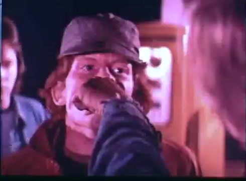 The still from the 'Last American Hero' trailer features two characters in a tense moment. One character, with red hair and wearing a cap, appears to be receiving an intense gesture or confrontation from another character who is partially out of focus. The setting suggests a dramatic or escalating situation, emphasizing themes of rivalry or conflict. The color palette looks muted, indicative of the film's era.