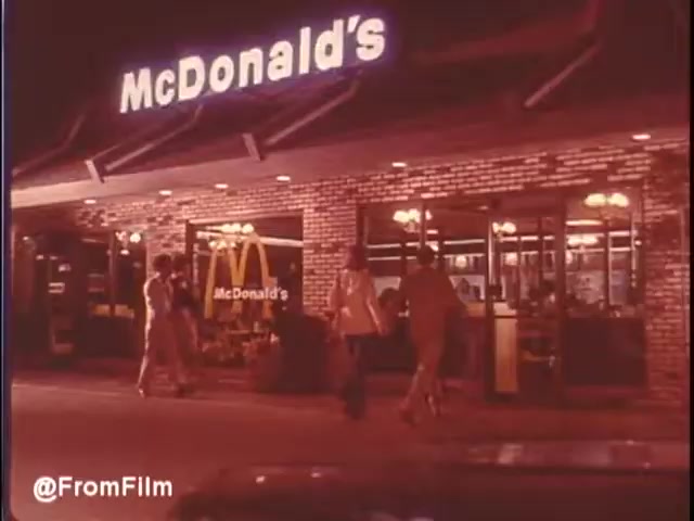 The still from the 1976 McDonald's commercial in New Orleans captures a vibrant nighttime scene outside a McDonald's restaurant. The iconic golden arches are prominently featured above the entrance, with a welcoming brick facade illuminated by warm lights. A small group of people is seen approaching the entrance, suggesting a lively atmosphere. The setting evokes a sense of nostalgia, reflecting both the era and the appeal of fast food culture at that time. The film's vintage quality adds to its charm.   Would I eat at McDonald's in New Orleans? Maybe...   Follow us on Twitter @FromFilm.